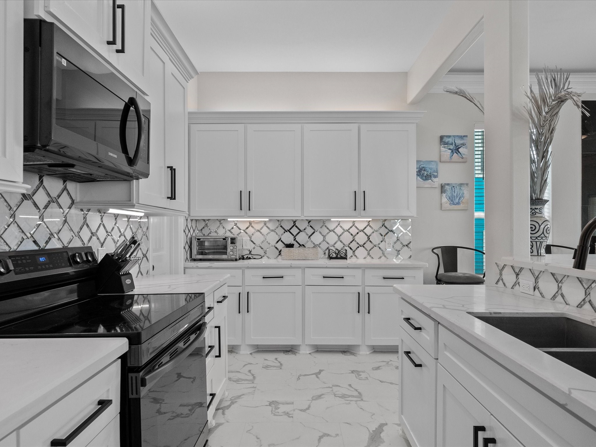 1018 Seashell Drive Surfside Beach, TX 77541 - Photo 15 of 49 This modern kitchen features sleek white cabinetry, a stylish black and white tile backsplash, and matching appliances. The bright, open layout is complemented by marble-style flooring, creating a clean and inviting space.