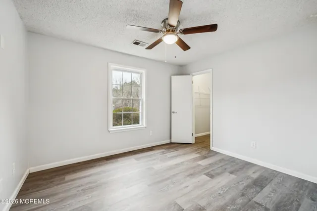 an empty room with wooden floor fan and windows