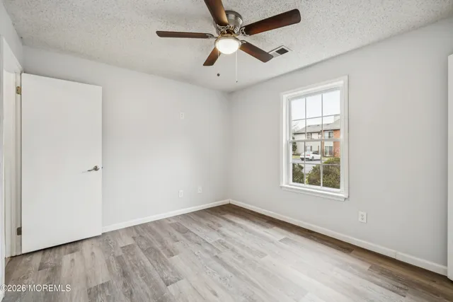 an empty room with wooden floor ceiling fan and windows