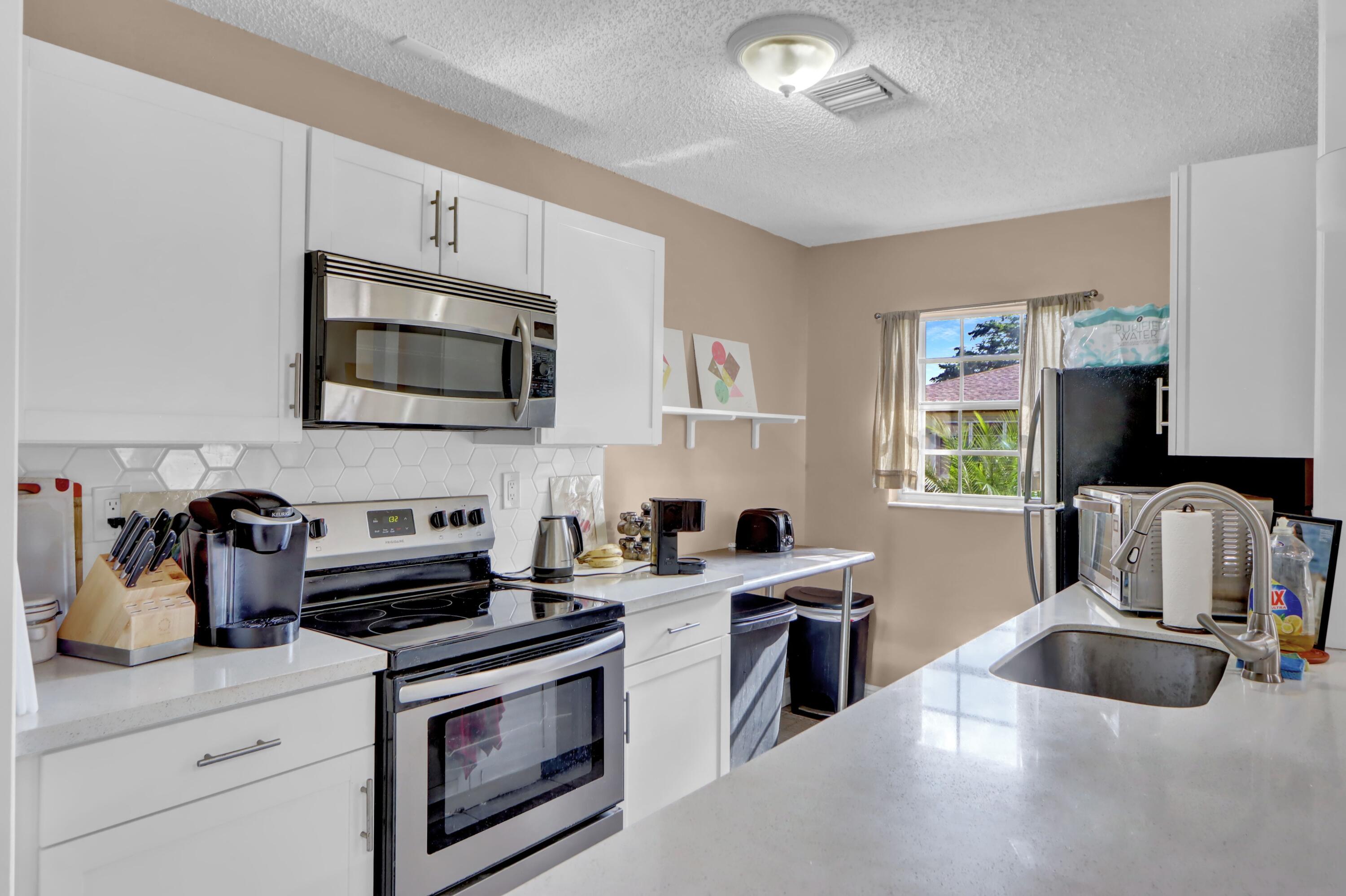 14050 Nesting Way, Unit B Delray Beach, FL 33484 - Photo 10 of 17 a kitchen with stainless steel appliances a stove a sink a microwave and cabinets