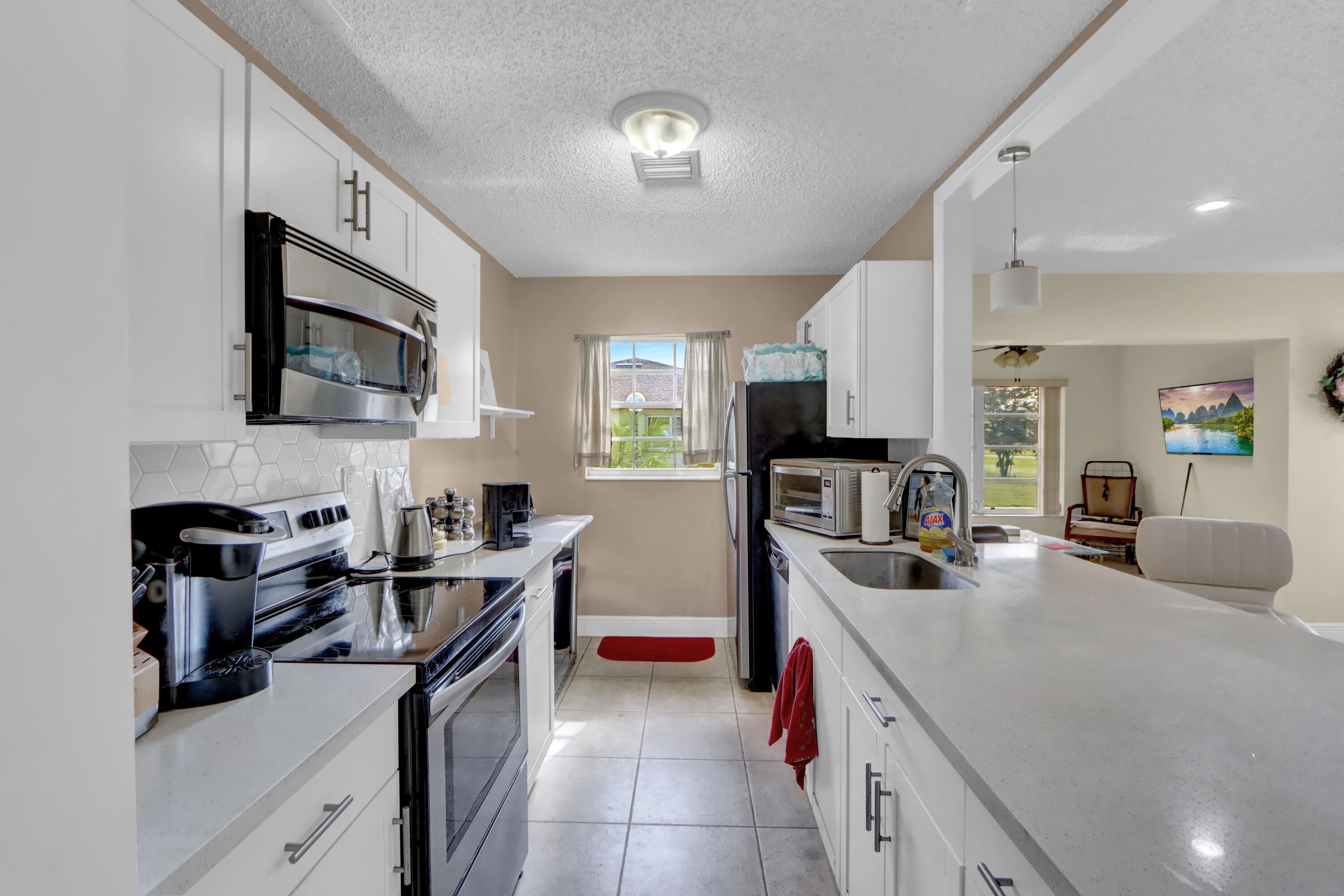 14050 Nesting Way, Unit B Delray Beach, FL 33484 - Photo 9 of 17 a kitchen with stainless steel appliances granite countertop a sink stove microwave and cabinets