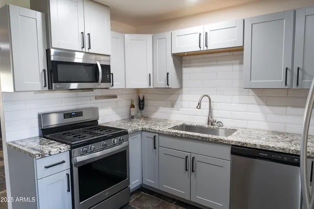 a kitchen with granite countertop a sink dishwasher a stove and a microwave oven with cabinets