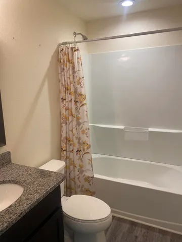 a bathroom with a granite countertop bathtub shower sink vanity and toilet
