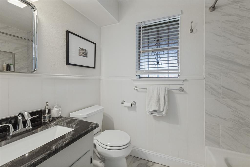9864 Shoreview Road Dallas, TX 75238 - Photo 19 of 24 Vanity with dark countertop and undermount sink, wainscoting, and tiled shower surround
