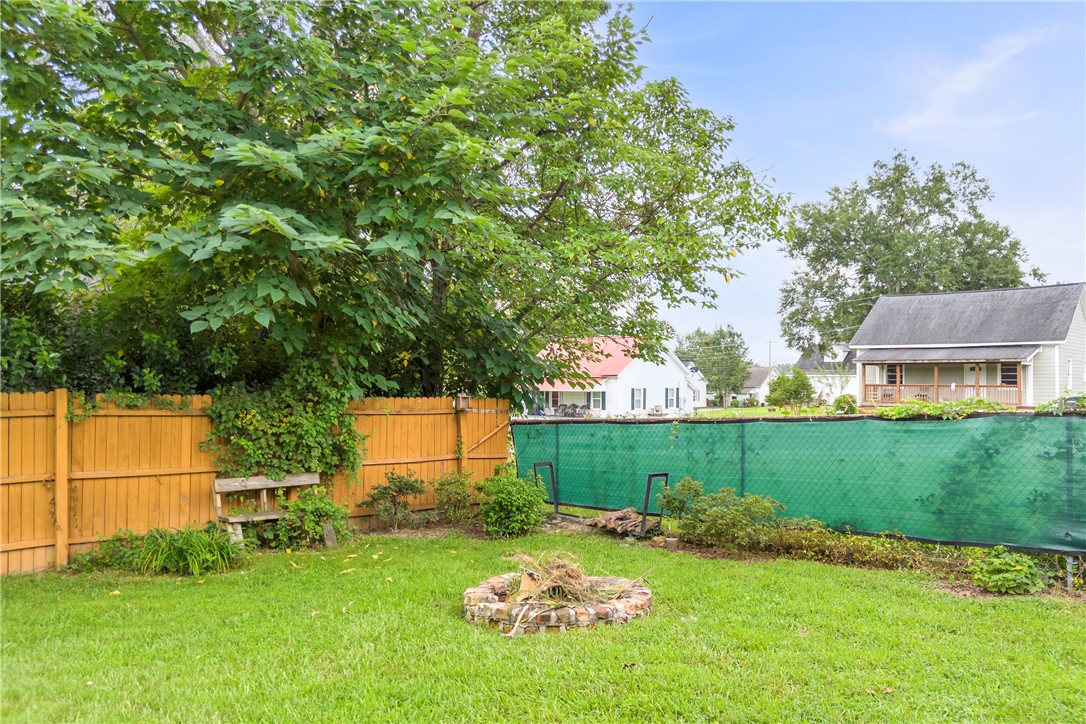 308 Verner Street Walhalla, SC 29691 - Photo 29 of 49 Mature trees shade a grassy lawn featuring a stone fire pit enclosed by wooden fencing.