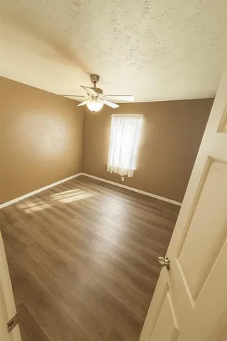 an empty room with wooden floor fan and windows
