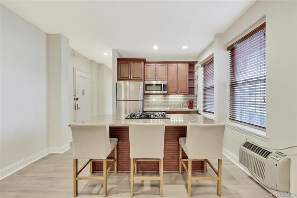 a kitchen with stainless steel appliances granite countertop a stove a sink a refrigerator white cabinets and chairs with wooden floor