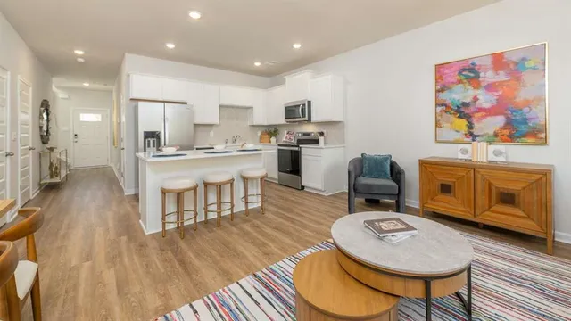 a living room with stainless steel appliances furniture a rug and a kitchen view
