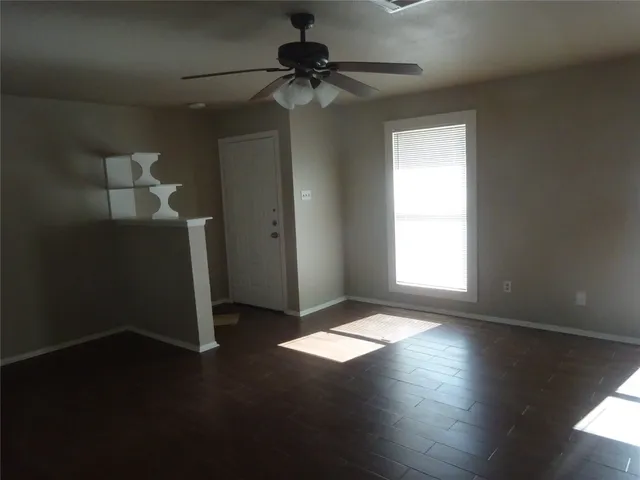 an empty room with wooden floor fan and windows