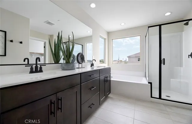 a bathroom with a double vanity sink a mirror a bathtub and next to a window