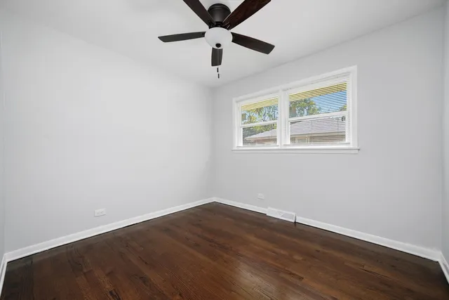 a view of an empty room with wooden floor and a ceiling fan