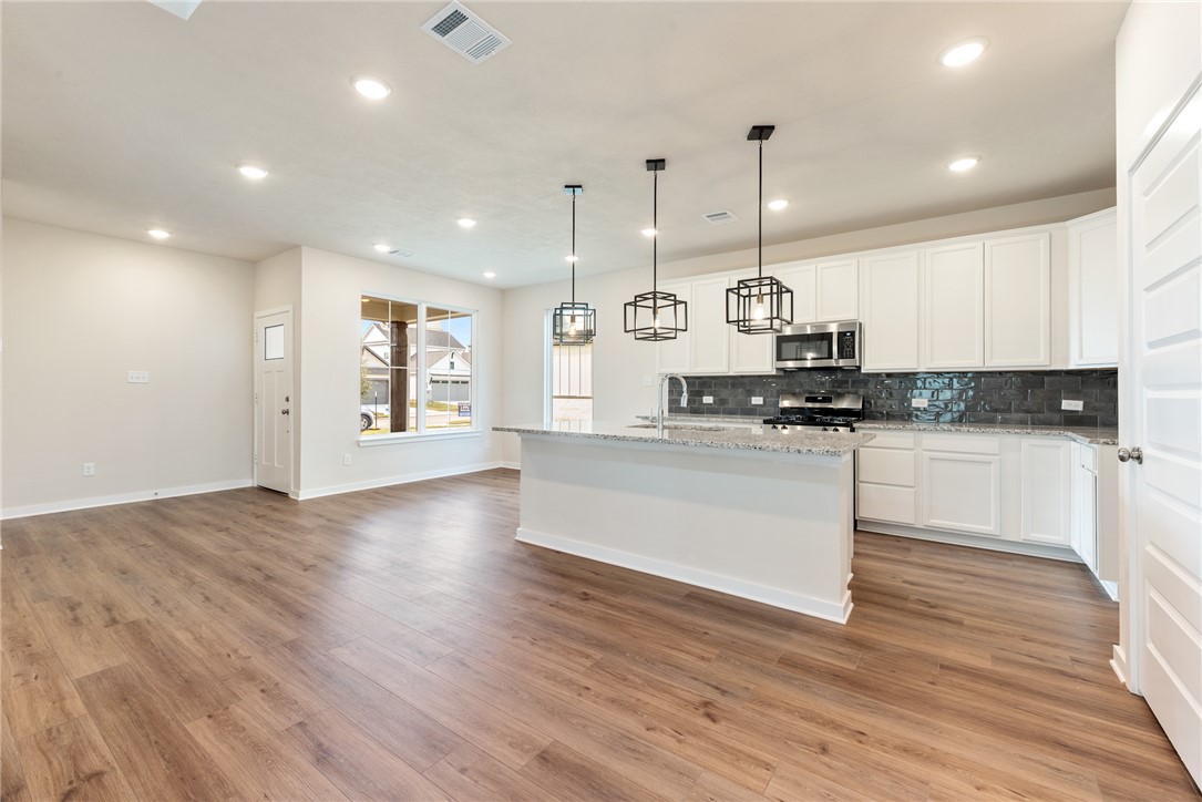 15238 Still Water Mdw Loop Bryan, TX 77845 - Photo 11 of 50 a large kitchen with stainless steel appliances granite countertop a stove a sink and white cabinets with wooden floor