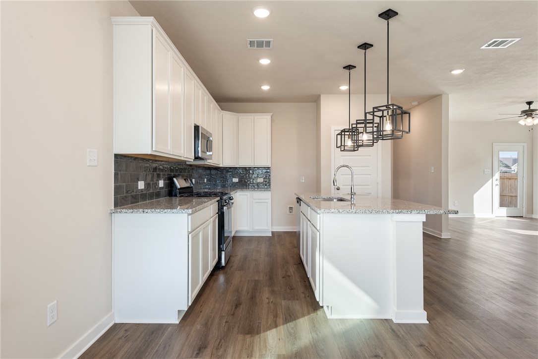 15238 Still Water Mdw Loop Bryan, TX 77845 - Photo 14 of 50 a kitchen with kitchen island stainless steel appliances a refrigerator a sink dishwasher a stove and white cabinets with wooden floor