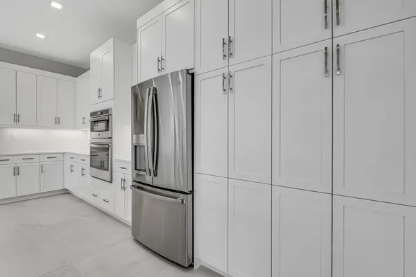 a large white kitchen with stainless steel appliances kitchen island a stove a sink a refrigerator and white cabinets