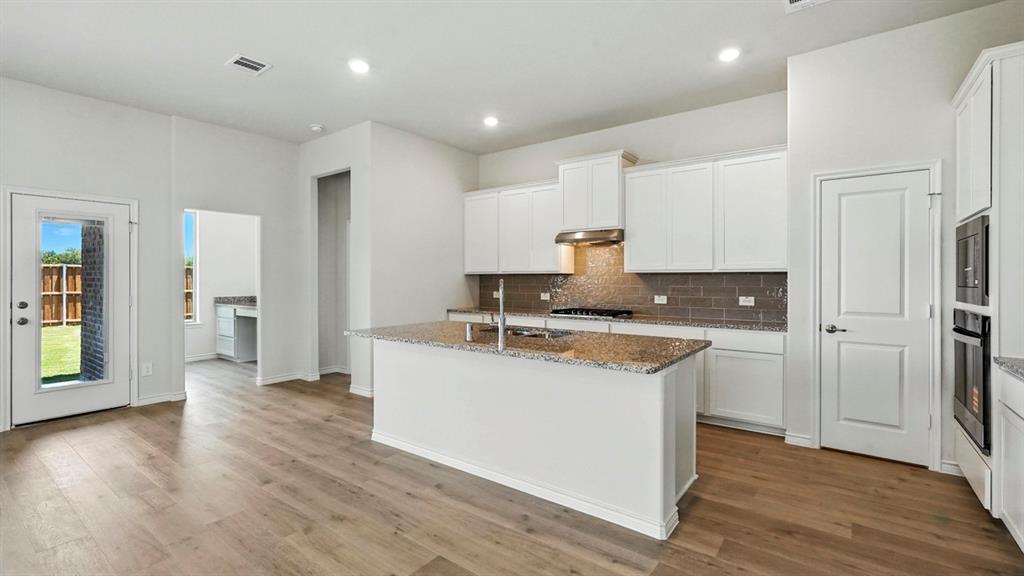 4191 Waldron Trail Forney, TX 75126 - Photo 5 of 20 Modern kitchen featuring a central island with a sink, white cabinetry, integrated stainless steel appliances, and wood-finish flooring