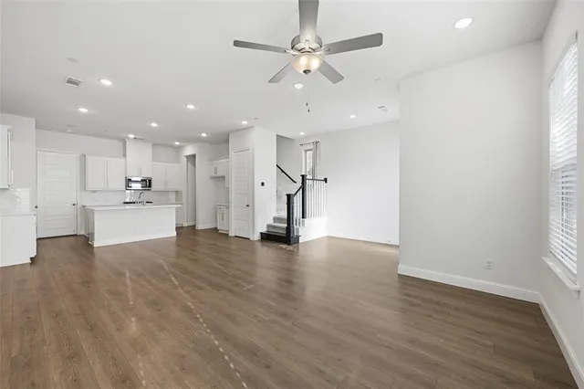 an empty room with wooden floor an kitchen view and a chandelier