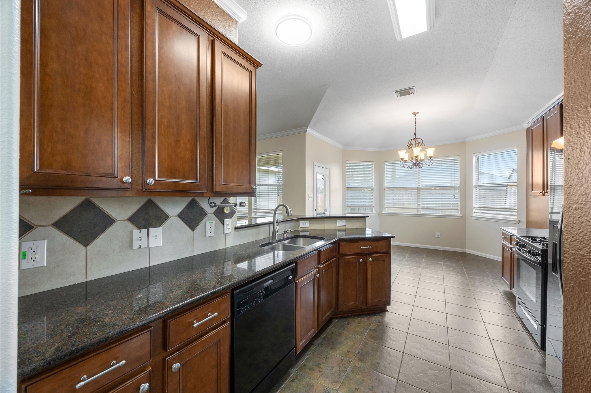 24538 Fort Settlement Drive Spring, TX 77373 - Photo 12 of 29 This kitchen features dark wood cabinets, granite countertops, and a tile backsplash. It includes modern appliances, ample natural light from large windows, and a dining area with a chandelier, offering a spacious and inviting atmosphere.