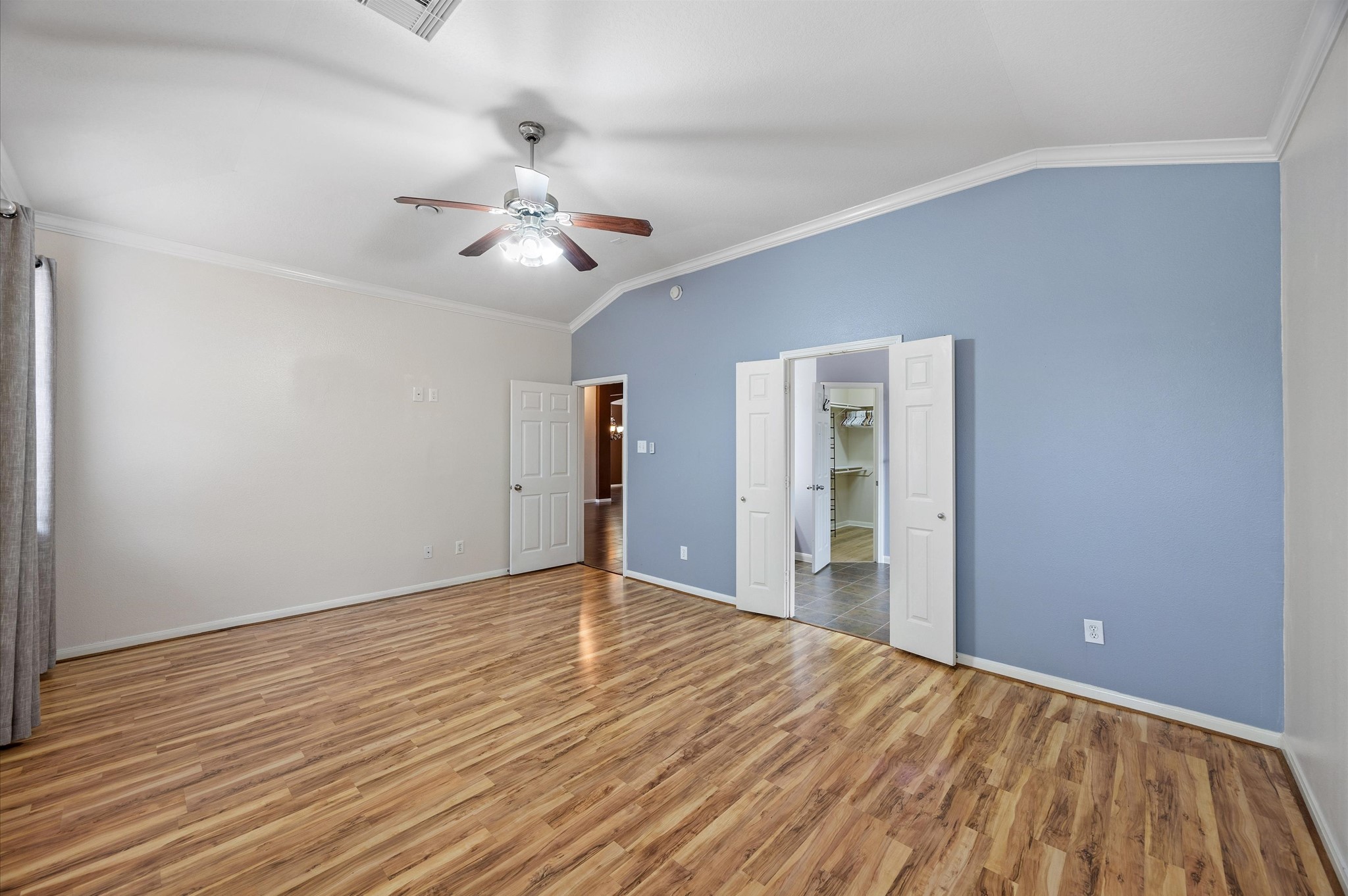 24538 Fort Settlement Drive Spring, TX 77373 - Photo 16 of 29 This spacious room features laminate wood flooring, a ceiling fan, and a soothing blue accent wall. It includes double doors leading to a walk-in closet and bathroom, offering a modern and airy feel.