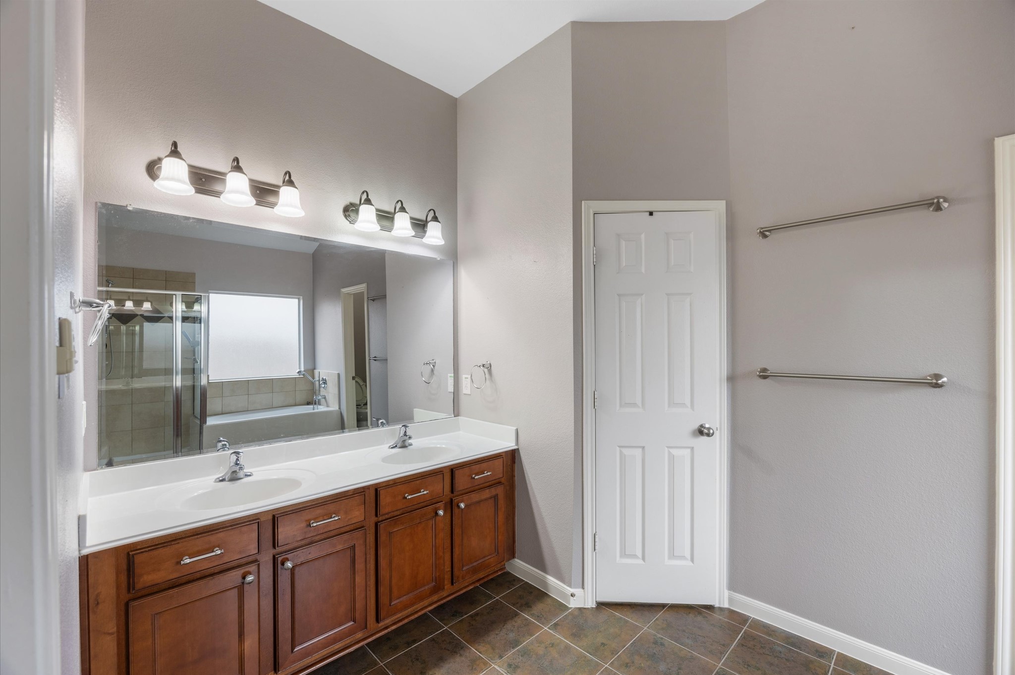 24538 Fort Settlement Drive Spring, TX 77373 - Photo 18 of 29 This bathroom features a double vanity with elegant wood cabinets, a large mirror, modern light fixtures, and a neutral color scheme. It includes towel racks and a door leading to additional storage or space, complemented by tiled flooring.