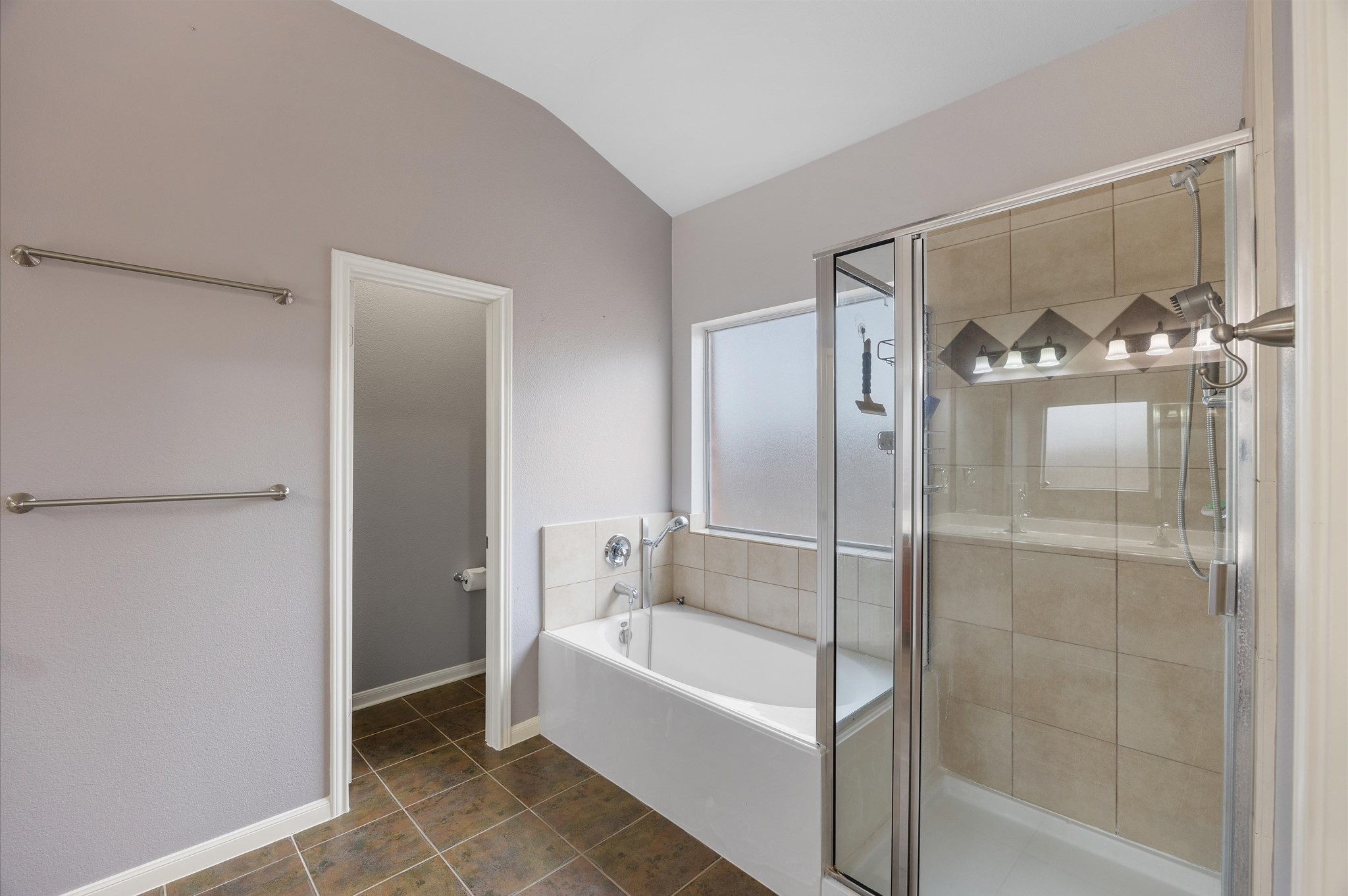 24538 Fort Settlement Drive Spring, TX 77373 - Photo 19 of 29 This bathroom features a modern design with a separate glass-enclosed shower, a spacious bathtub, neutral tile flooring, and ample natural light from a frosted window. Towel racks are conveniently placed, and there's a door leading to a separate area.