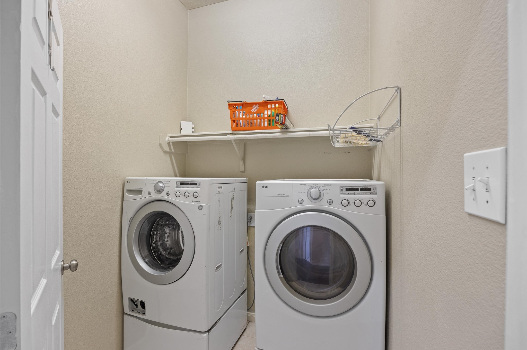 24538 Fort Settlement Drive Spring, TX 77373 - Photo 23 of 29 Compact laundry room featuring a front-loading washer and dryer set. There's a shelf above for storage, providing convenient organization for laundry supplies.