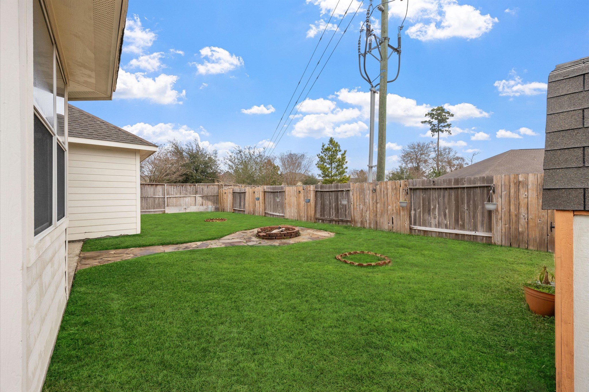 24538 Fort Settlement Drive Spring, TX 77373 - Photo 26 of 29 This photo showcases a well-maintained backyard with lush green grass, a wooden fence for privacy, and a small paved area. There are utility poles visible, adding a suburban feel. Ideal for outdoor activities and relaxation.