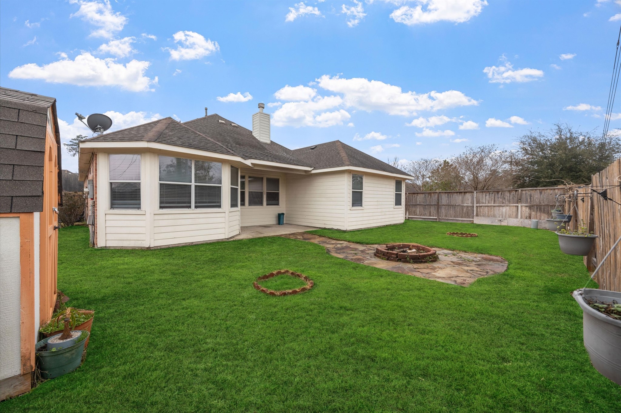 24538 Fort Settlement Drive Spring, TX 77373 - Photo 28 of 29 This photo showcases a charming backyard with lush green grass, a small wooden shed, and a cozy patio area featuring a built-in fire pit. The house exterior is a light color and features a fenced perimeter, offering privacy and a welcoming outdoor space.
