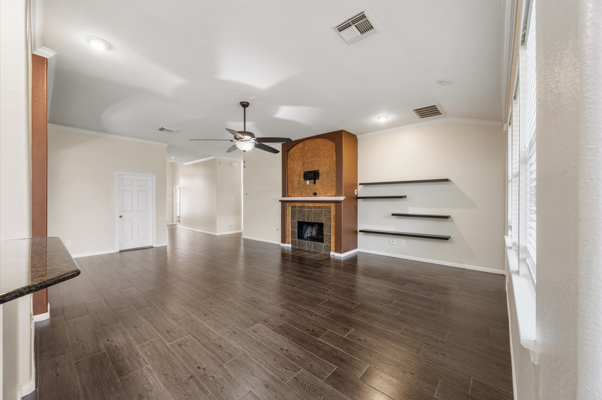 24538 Fort Settlement Drive Spring, TX 77373 - Photo 6 of 29 Spacious living area with dark wood flooring, a cozy fireplace, and modern floating shelves. Ceiling fan and ample natural light create a warm and inviting atmosphere.