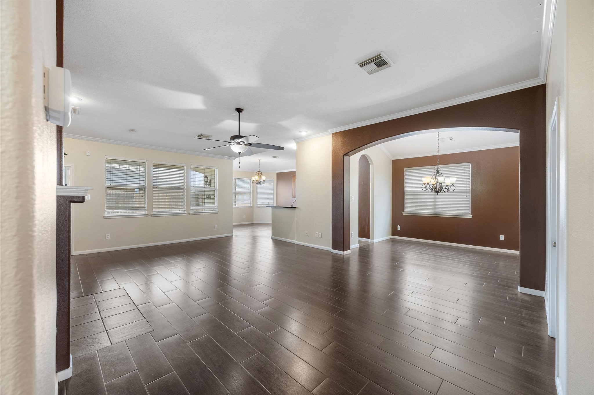24538 Fort Settlement Drive Spring, TX 77373 - Photo 7 of 29 This open-concept living space features dark hardwood floors, ample natural light from multiple windows, and a central ceiling fan. The room connects seamlessly to a dining area with an elegant chandelier and an arched entryway. Neutral walls provide a versatile backdrop for any decor style.