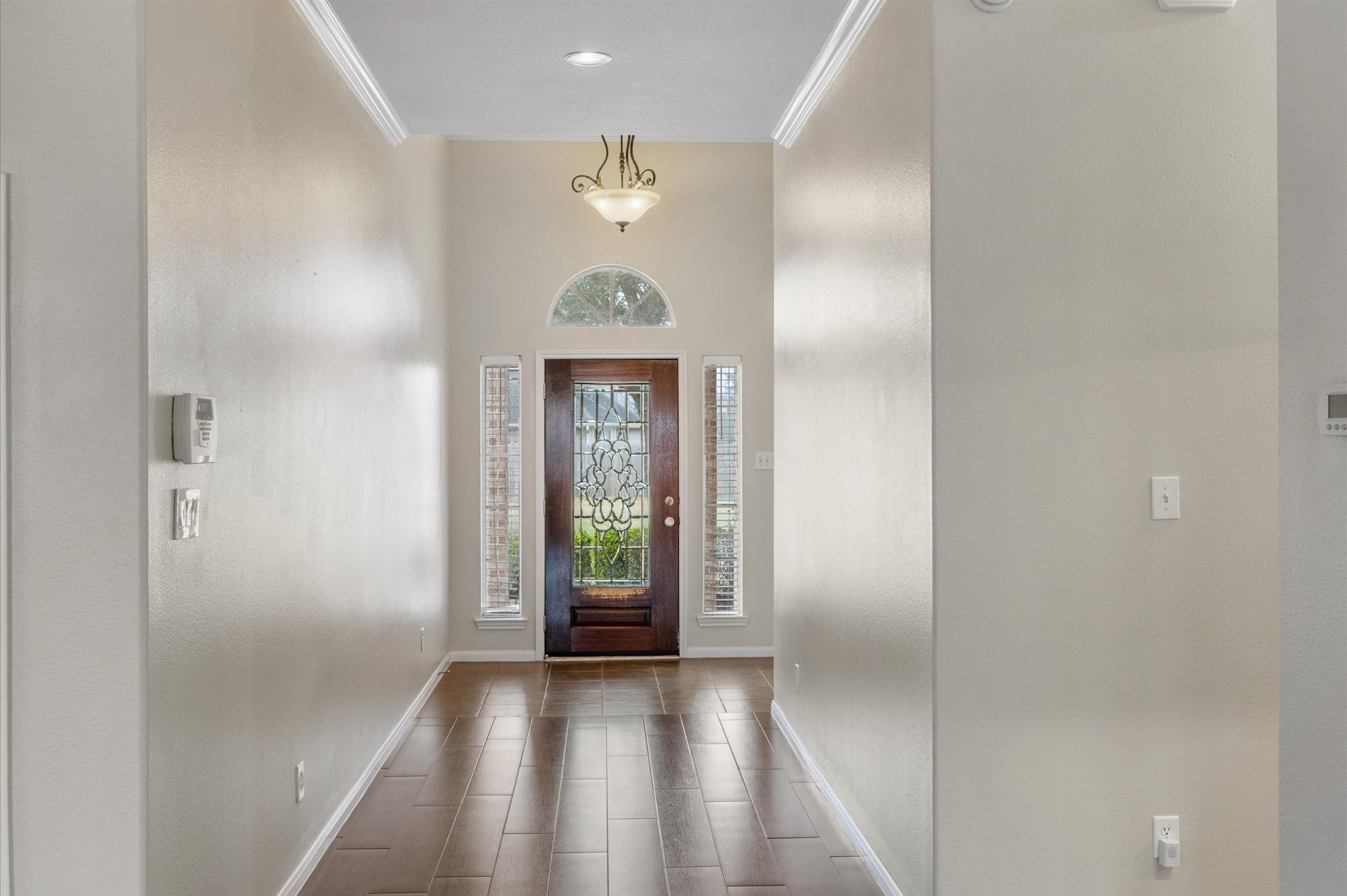 24538 Fort Settlement Drive Spring, TX 77373 - Photo 8 of 29 Bright and welcoming entryway with high ceilings, crown molding, and elegant lighting. The space features a beautifully detailed wooden front door with glass panels and side windows, allowing natural light to fill the hallway.