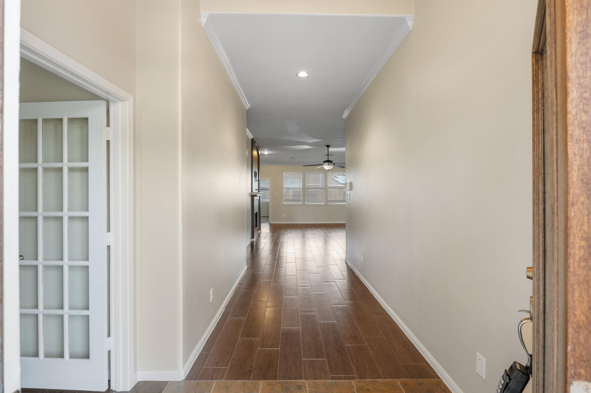 24538 Fort Settlement Drive Spring, TX 77373 - Photo 9 of 29 This photo shows a welcoming entryway with a long hallway leading to a bright living space. It features neutral walls, wood-look flooring, and a ceiling fan, creating a warm and inviting atmosphere. French doors on the left suggest access to an additional room.