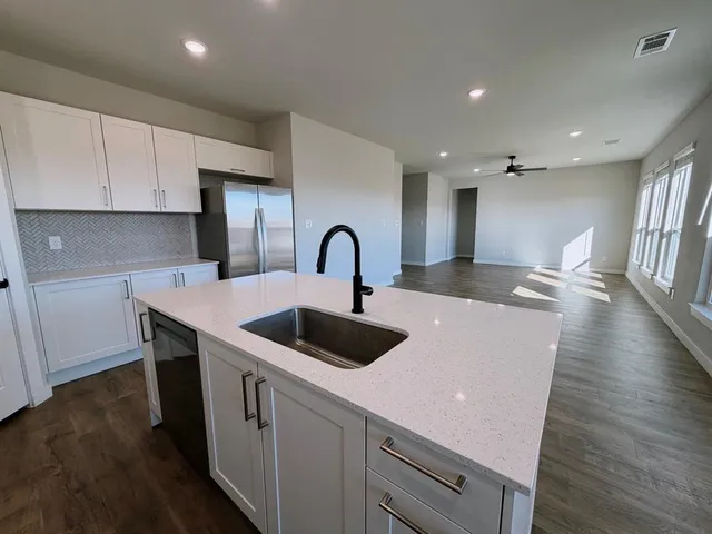 a large kitchen with stainless steel appliances a sink a stove a refrigerator and white cabinets