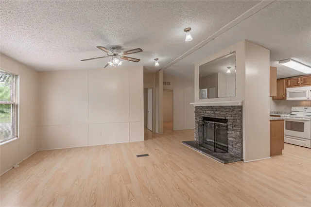 an empty room with windows fireplace and a kitchen view