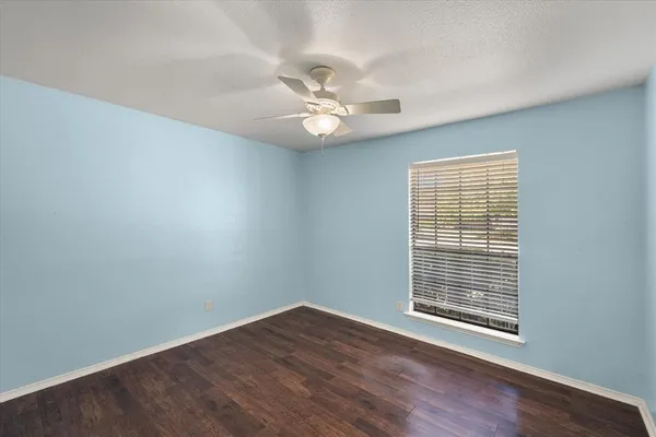 an empty room with wooden floor ceiling fan and windows