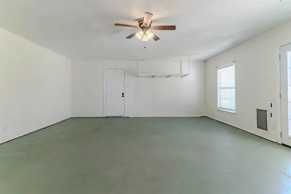 an empty room with chandelier fan and windows