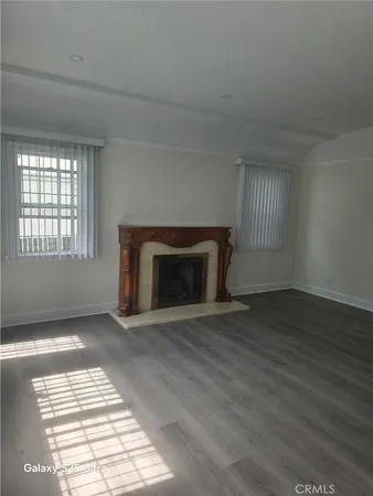 an empty room with wooden floor fireplace and windows