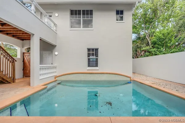 a view of a white house with a yard plants and a large tree