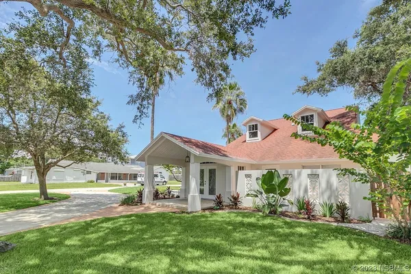 a front view of a house with a yard and potted plants and large trees