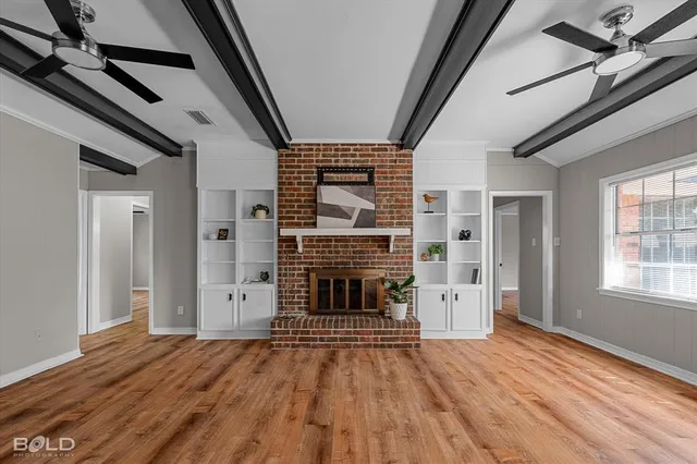 an empty room with wooden floor fireplace and windows