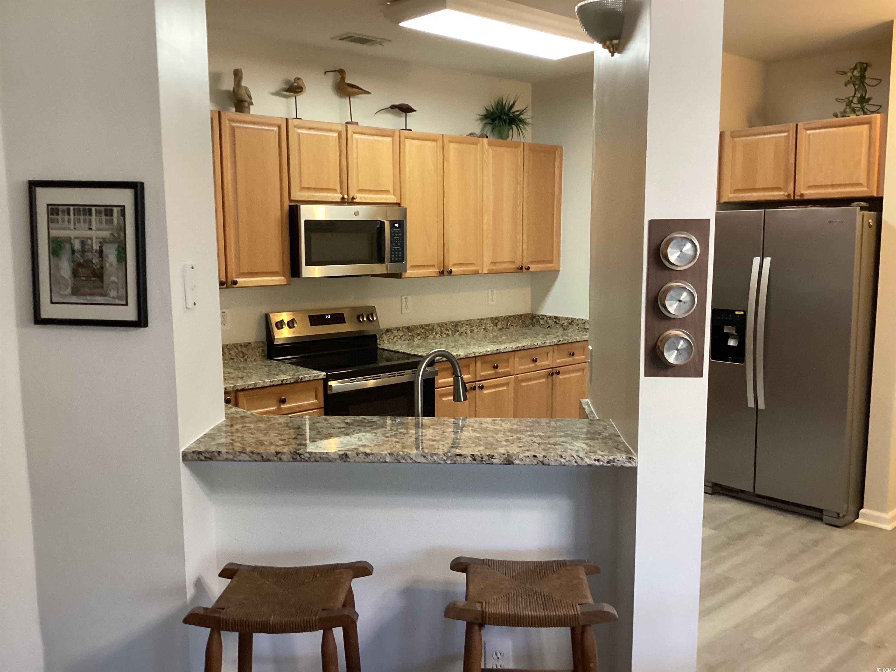 4430 Lady Banks Lane, Unit C1 Murrells Inlet, SC 29576 - Photo 6 of 34 Kitchen with stainless steel appliances, light stone countertops, light brown cabinets, light wood finished floors, and a kitchen breakfast bar
