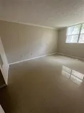 an empty room with windows and view of kitchen