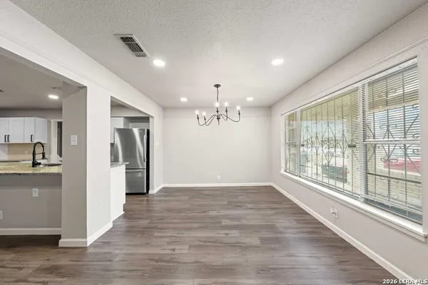 a view of an empty room with wooden floor and a kitchen