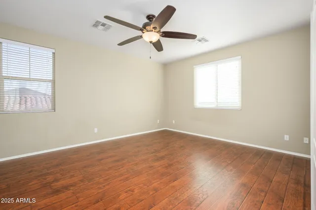 an empty room with wooden floor fan and windows