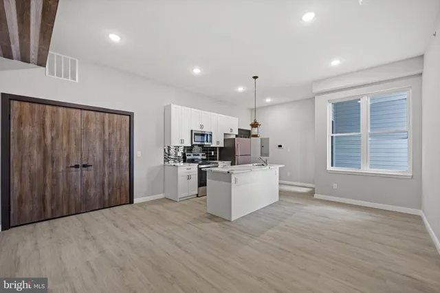 a large white kitchen with kitchen island a sink a center island stainless steel appliances and a window