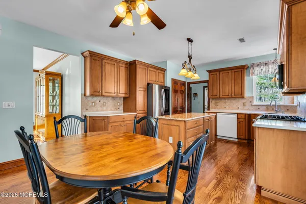 a kitchen with stainless steel appliances granite countertop wooden cabinets a stove a sink a dining table and chairs with wooden floor