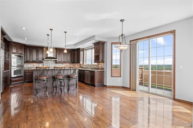 a kitchen with stainless steel appliances granite countertop a stove top oven a sink dishwasher a dining table and chairs with wooden floor