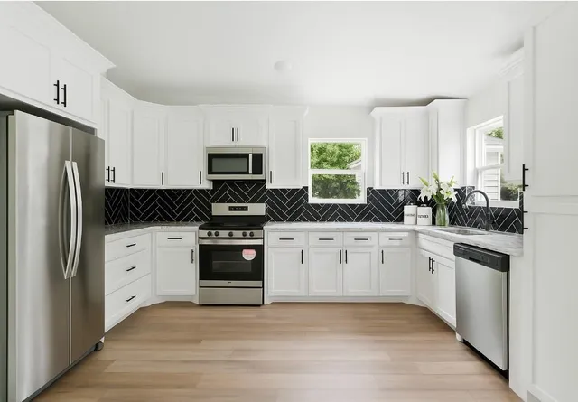 a white kitchen with stainless steel appliances granite countertop a stove a sink and a refrigerator