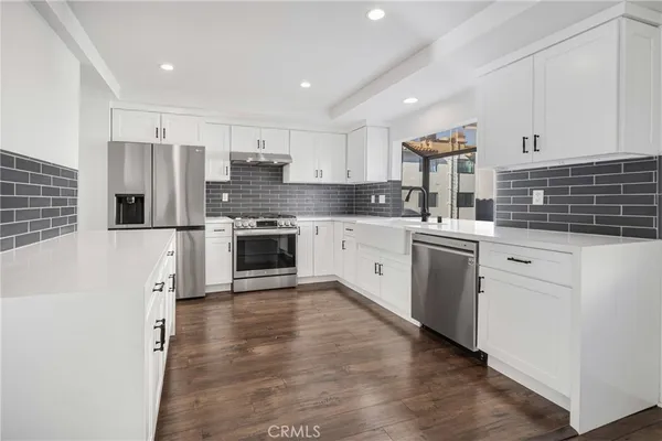 a kitchen with stainless steel appliances kitchen island granite countertop a refrigerator oven a sink dishwasher and white cabinets with wooden floor