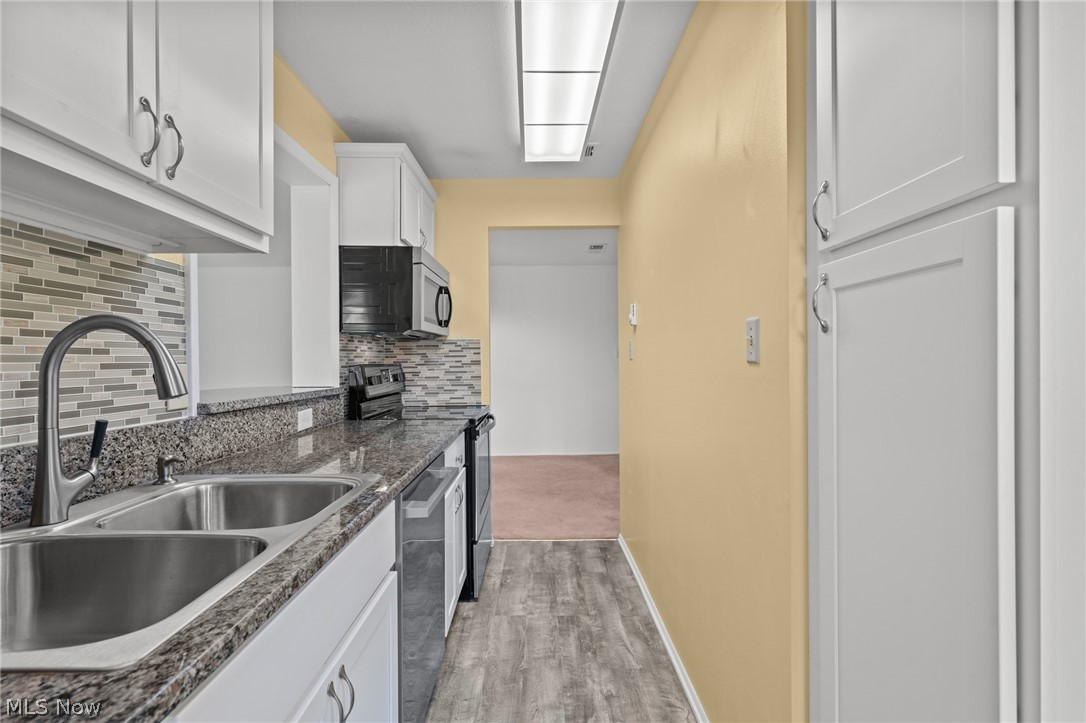3070 Kent Road, Unit 312D Stow, OH 44224 - Photo 21 of 49 Galley kitchen featuring white cabinetry with chrome hardware, granite-style countertops, stainless steel double-basin sink with gooseneck faucet, mosaic tile backsplash, and wood-finish flooring throughout