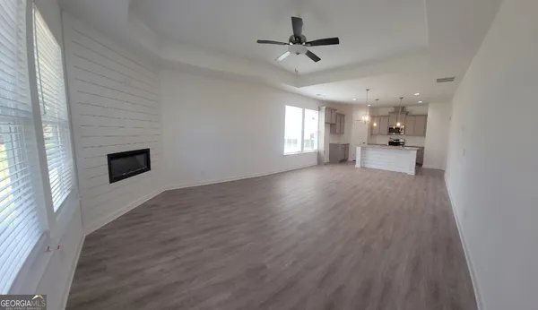 a view of a big room with wooden floor a ceiling fan and windows